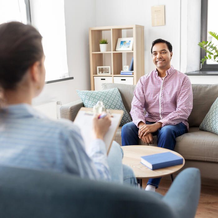 psychology, mental therapy and people concept - happy smiling young indian man patient and woman psychologist at psychotherapy session